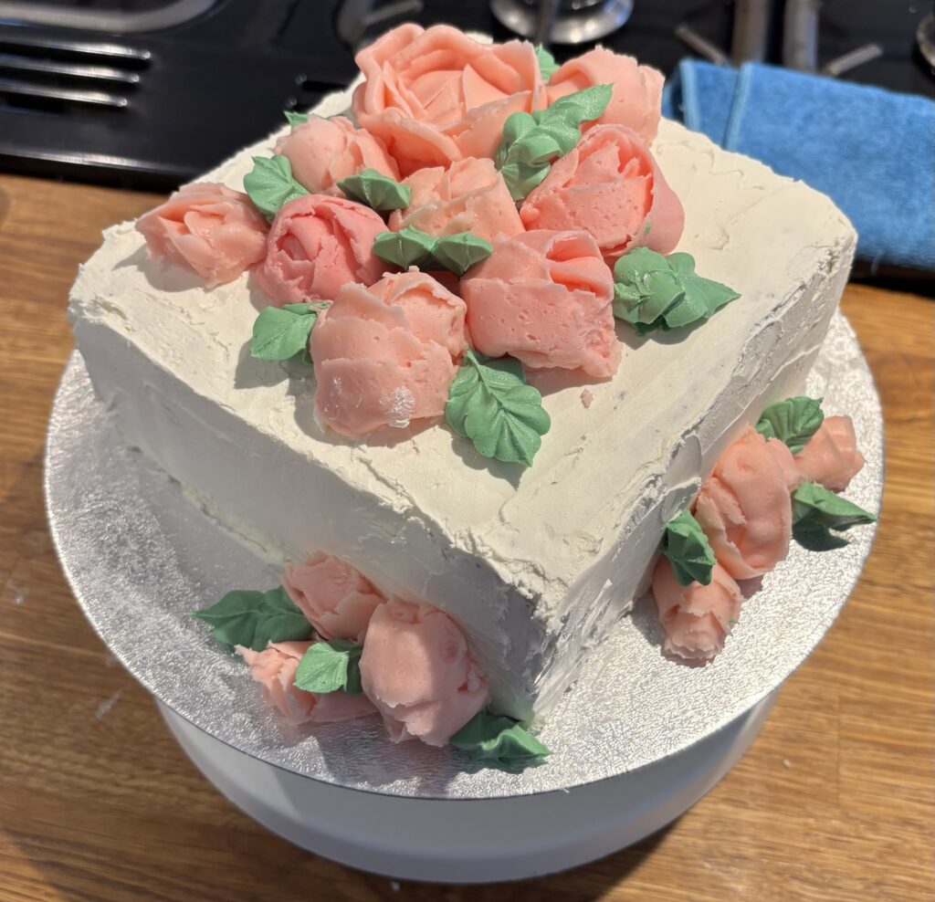 Fruitcake with two coats of vanilla buttercream icing, decorated with strawberry flavoured pink roses and leaves. 